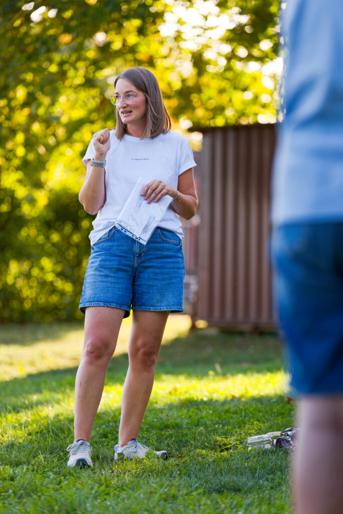 Hundetrainerin Karin erklärt den Teilnehmenden einer Trainingsstunde auf einer Wiese einen Trainingsinhalt